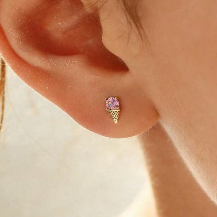 A close-up of a person's ear wearing a small gold stud earring with a lavender-purple gemstone set in a textured cone design.