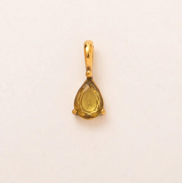 A small gold pendant with a teardrop-shaped yellow gemstone in a prong setting, shown on a plain off-white background.