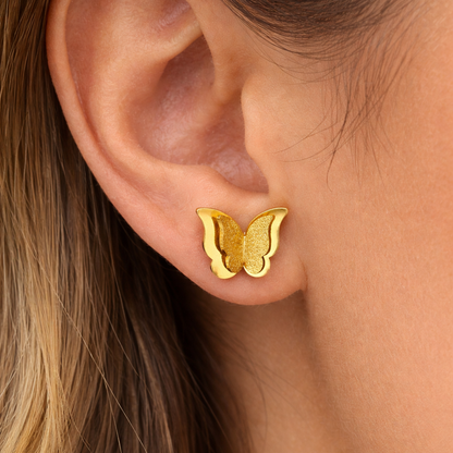 A close-up of a person's ear wearing a small gold butterfly stud earring.