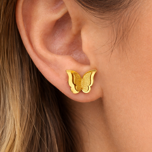 A close-up of a person's ear wearing a small gold butterfly stud earring.