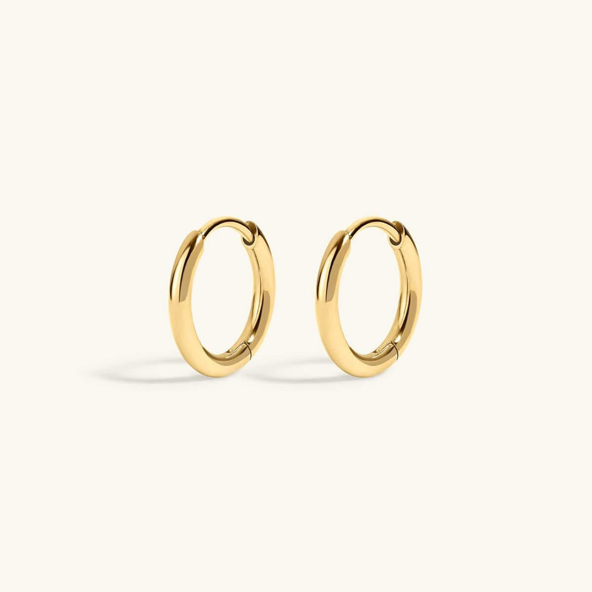A pair of polished gold huggie hoop earrings on a clean, off-white background.