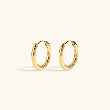 A pair of polished gold huggie hoop earrings on a clean, off-white background.