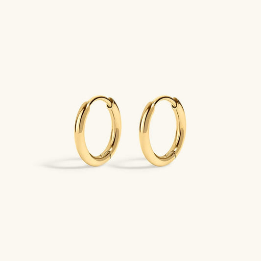 A pair of polished gold huggie hoop earrings on a clean, off-white background.