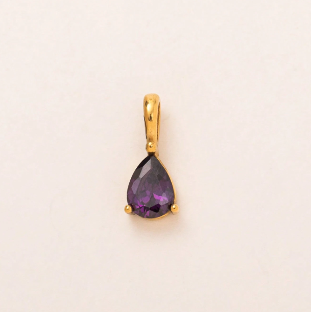 A gold pendant featuring a teardrop-shaped purple gemstone, photographed on a plain off-white background.