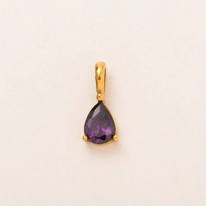 A gold pendant featuring a teardrop-shaped purple gemstone, photographed on a plain off-white background.