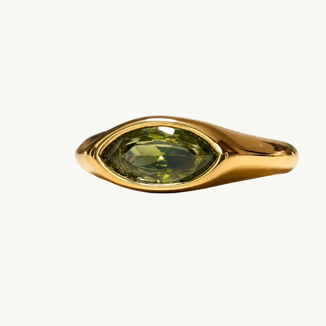 A gold ring featuring a marquise-cut olive green gemstone, displayed on a clean, light beige reflective surface.