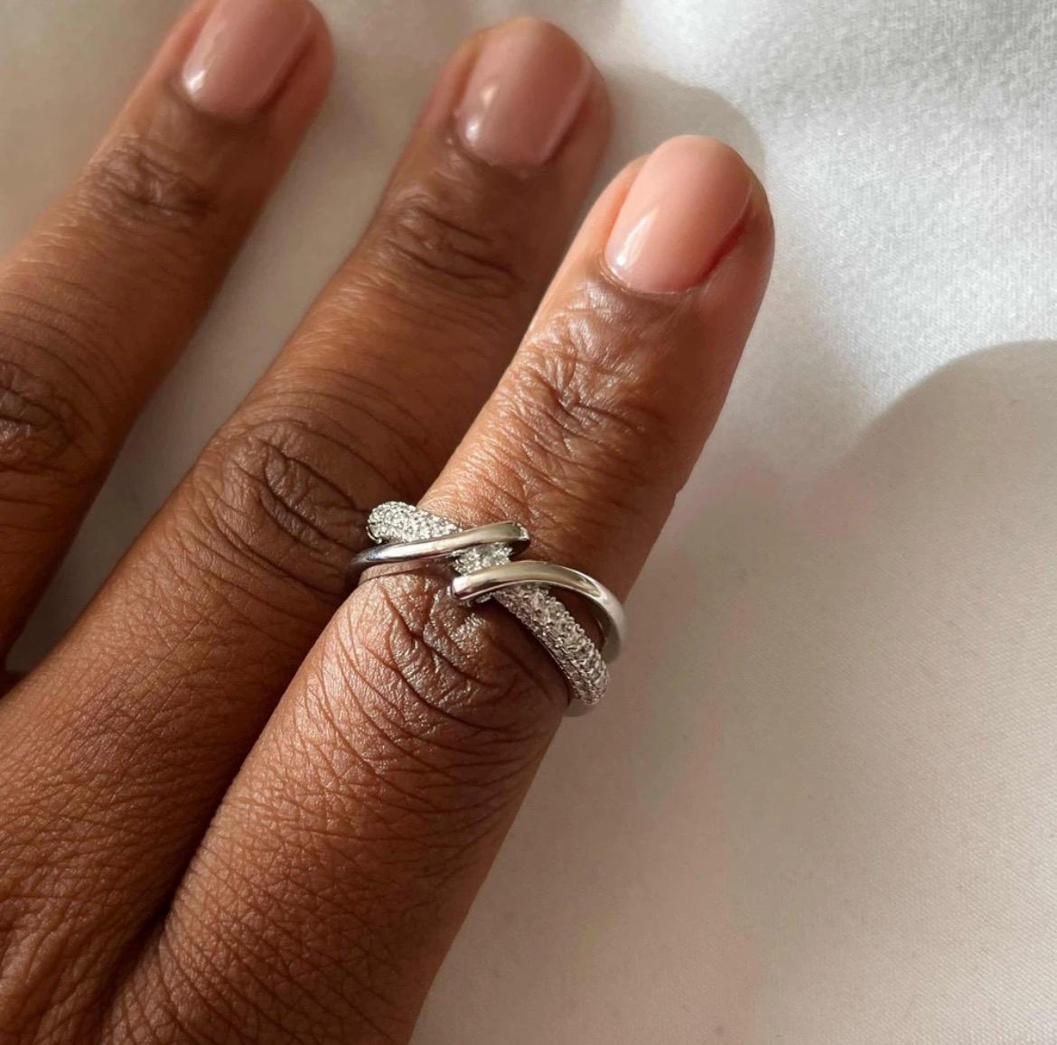 A close-up of a hand wearing two silver rings with pavé-set clear stones, resting on a light neutral surface.