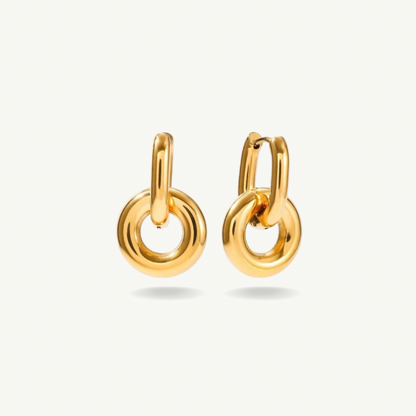 A pair of polished gold huggie hoop earrings with integrated circular drop charms, shown on a clean off-white background.