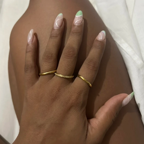 Three thin gold rings worn on a person's hand, shown against skin with manicured nails and a white fabric background.