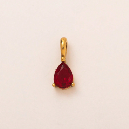 A gold pendant featuring a teardrop-shaped red gemstone in a prong setting, photographed against a plain off-white background.