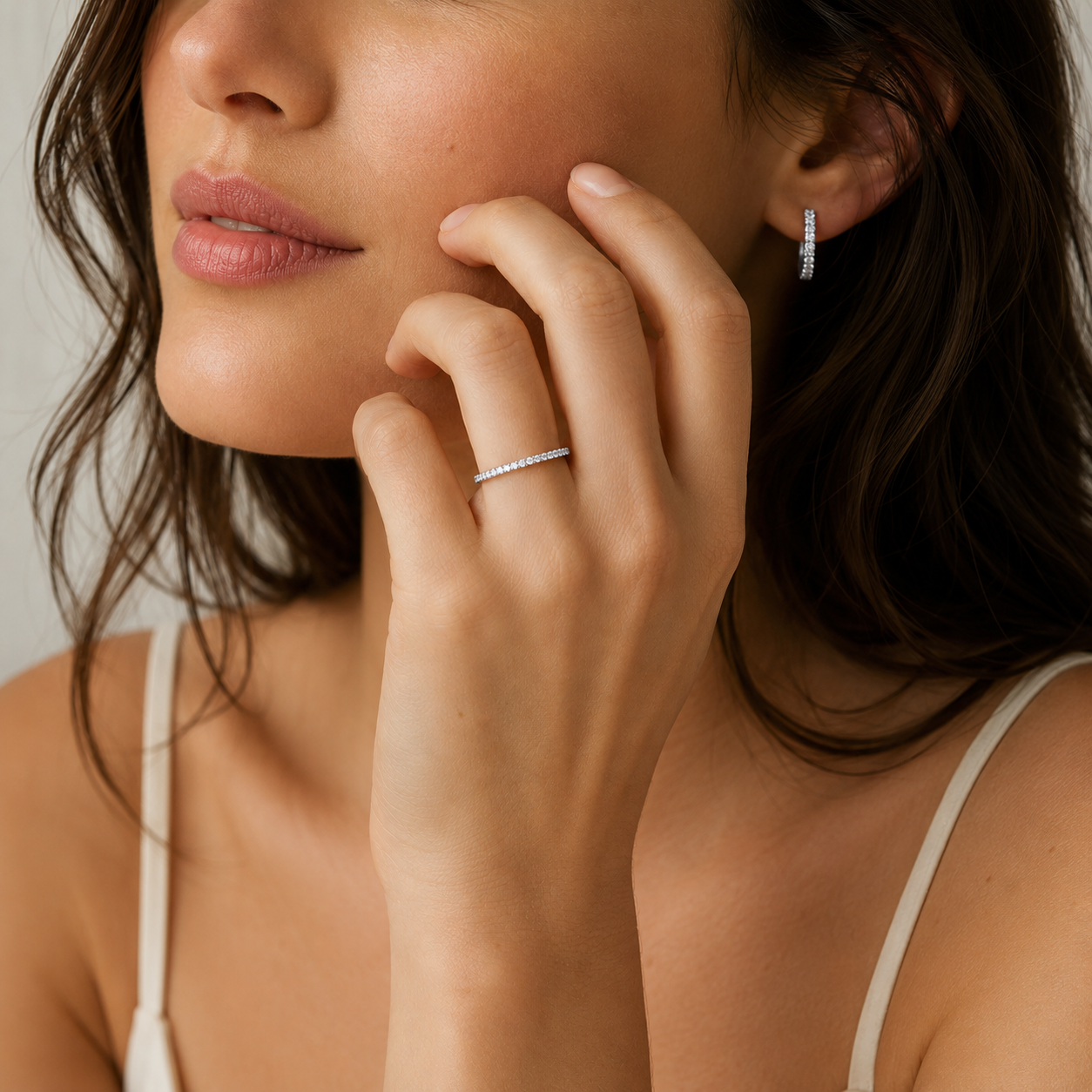 A close-up lifestyle shot of a woman wearing a delicate silver ring with small clear stones on her finger, alongside a matching small silver hoop earring.