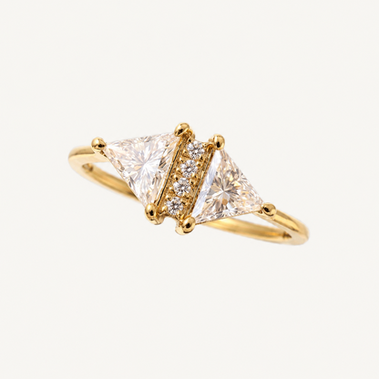 A yellow gold ring featuring two triangular clear gemstones flanked by a row of small round diamonds, set on a plain light background.