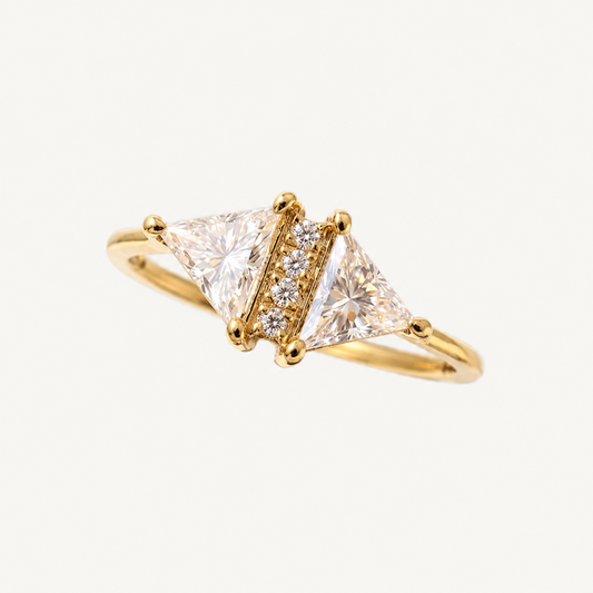 A yellow gold ring featuring two triangular clear gemstones flanked by a row of small round diamonds, set on a plain light background.