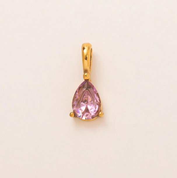 A gold pendant featuring a faceted pear-cut pink gemstone in a prong setting, centered on a plain off-white background.