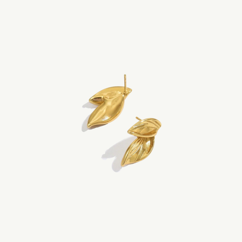 A pair of gold leaf-shaped stud earrings with textured detailing, shown on a clean off-white background.