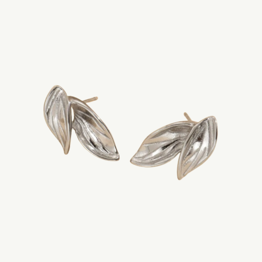 A pair of silver-toned leaf stud earrings with a textured, ribbed surface, displayed on a clean off-white background.