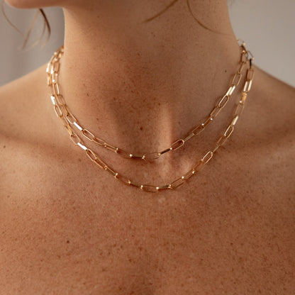 Gold chain necklace on a person's neck with a neutral background