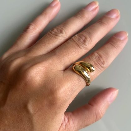 A close-up of a hand wearing a polished gold wrap ring, set against a plain light gray background.