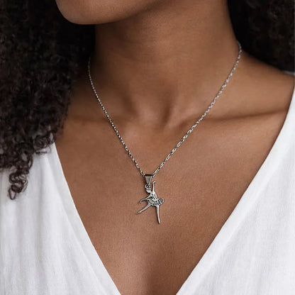 A close-up of a model wearing a silver-toned dandelion pendant necklace on a delicate chain, paired with a white V-neck top.