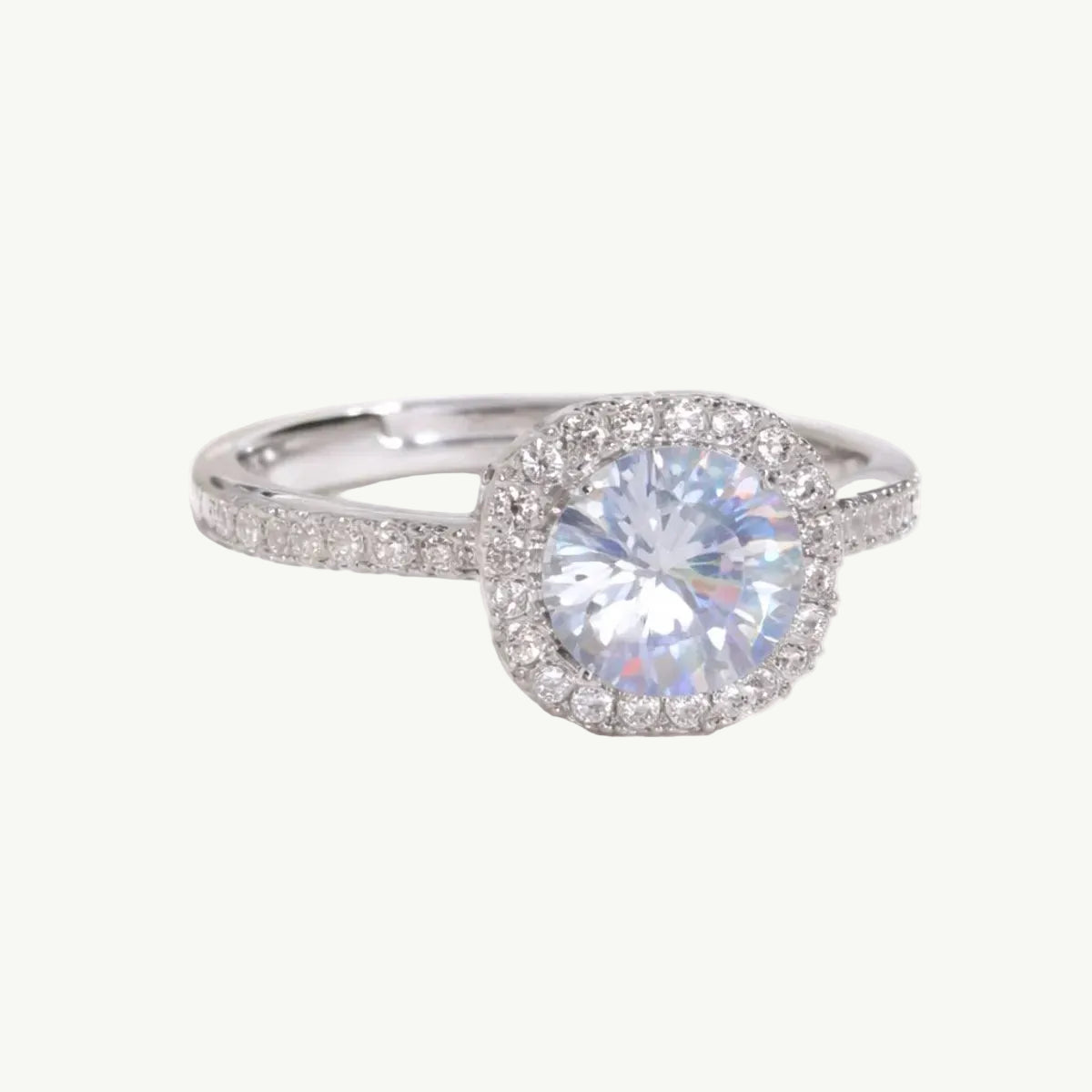 A silver halo engagement ring with a large round brilliant-cut center stone and smaller accent stones along the band, displayed on a soft white satin fabric.