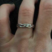 A silver infinity-style band ring worn on a person's ring finger, shown against a dark textured background.
