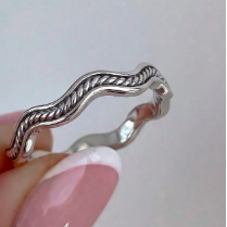A silver twisted rope band ring being worn on a hand with pink French-tipped nails, shown against a soft light gray background.
