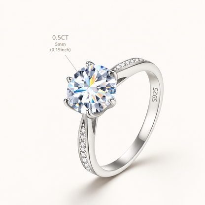 A silver solitaire engagement ring with a round brilliant-cut clear gemstone and a pavé-set band, shown on a light cream background with a size and carat callout overlay.