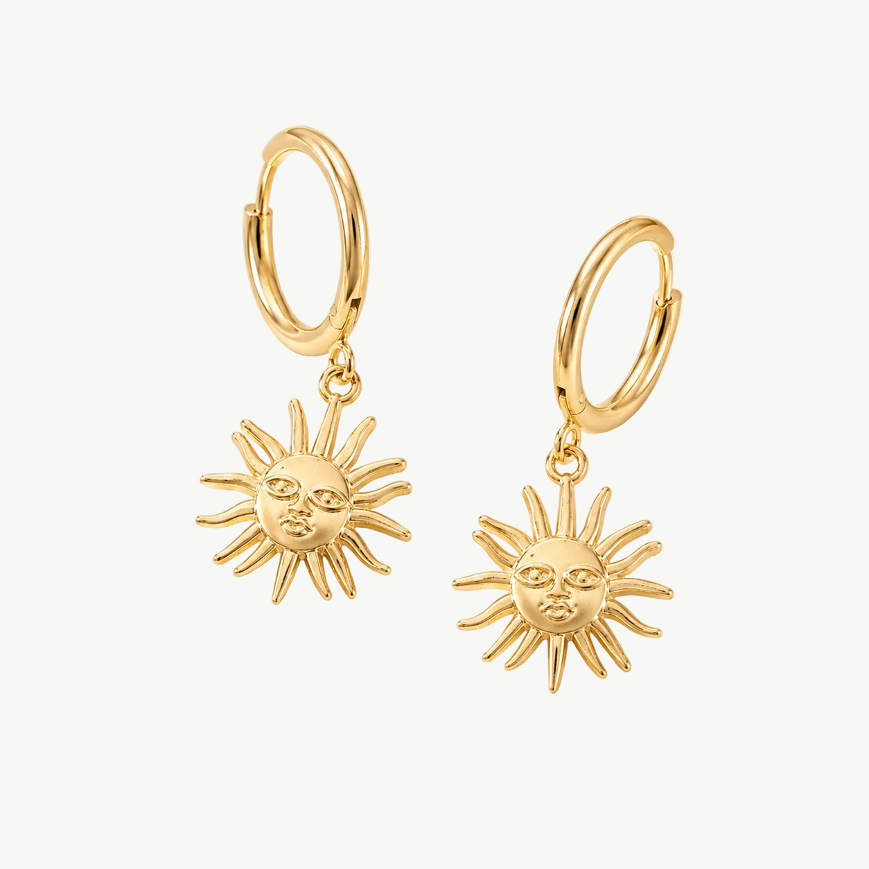 A pair of gold hoop earrings with dangling sun-face charms, displayed on a draped cream satin fabric background.