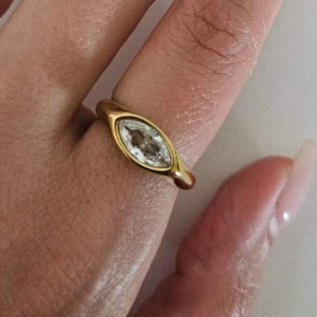 A close-up of a hand wearing a gold ring with a marquise-cut clear gemstone.