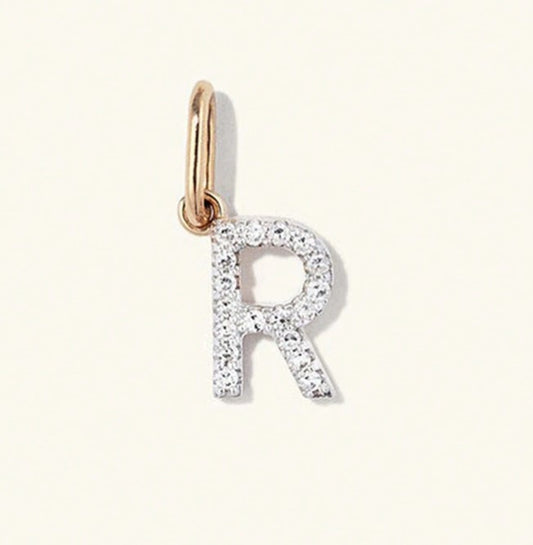 A close-up of a letter 'R' initial pendant charm, featuring a rose gold top loop and a silver-toned body paved with small clear stones, set against a solid off-white background.